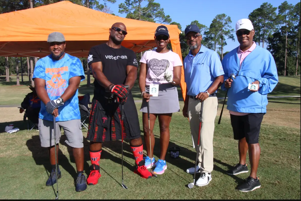 Cousin's Cup Golf Tournament @ Melanated Campout 15 Camp Cousins gathered with their clubs beside the orange tent, including a player in a Veteran shirt